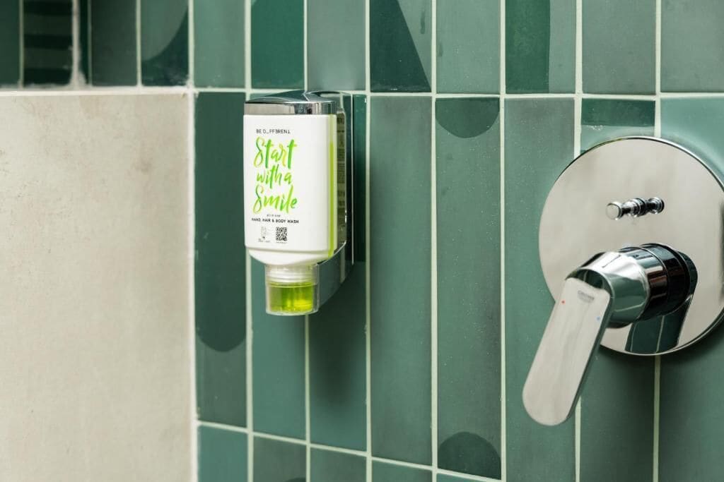 Une salle de bain avec des carreaux verts, un distributeur de savon liquide et un robinet.