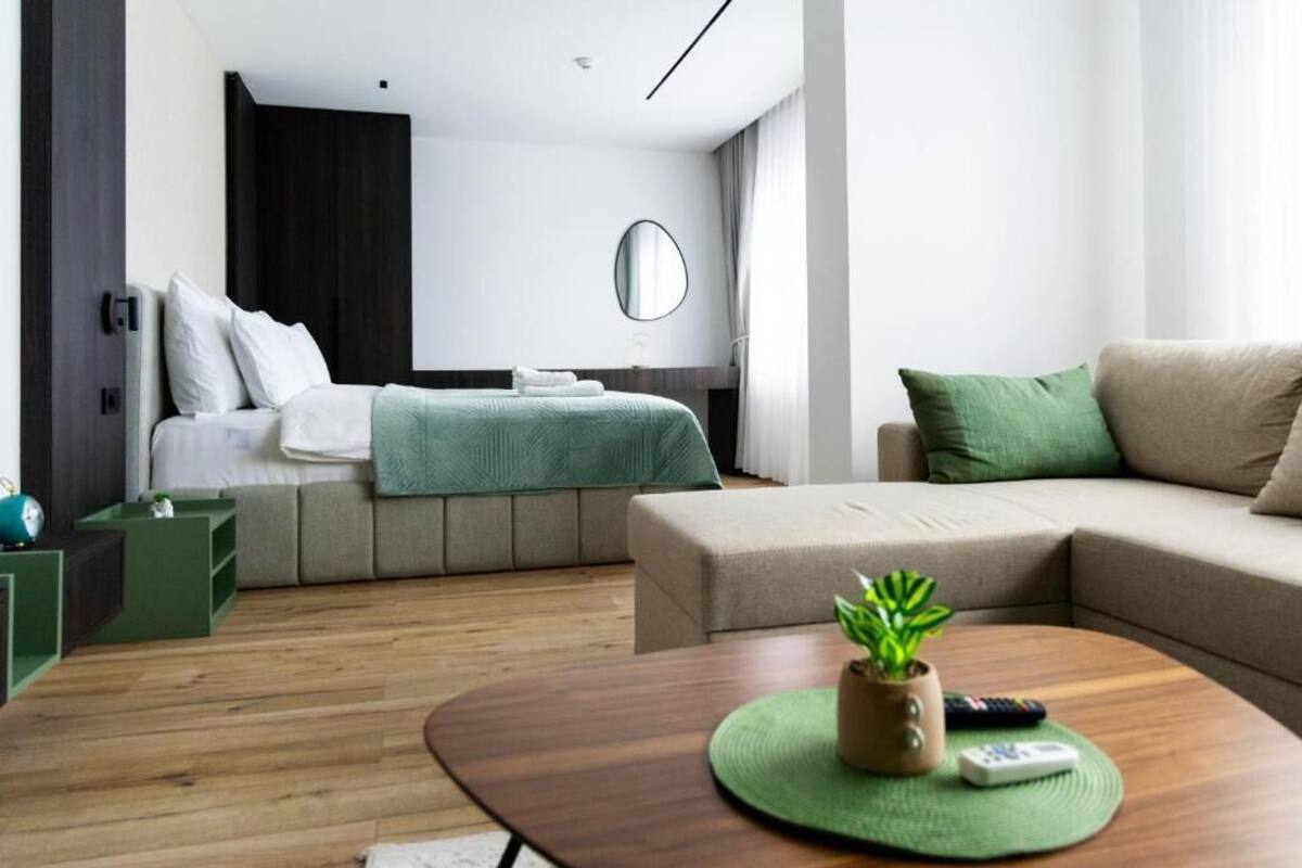 Moderni hotellihuone, jossa on sänky, sohva, kasvi koristeltuna kahvipöydällä ja peili seinällä.