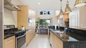 A modern kitchen with stainless steel appliances, wooden cabinets, a black granite countertop, and pendant lighting. - Last Minute Disney Getaway! Modern Townhome with Private Balcony. Book Now! #170017 (Orlando)