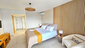 Ein modernes Hotelzimmer mit Bett, Nachttischen, einer Couch, einer Hängelampe und einer Wandpaneele aus Holz.