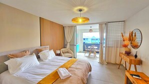 Ein Hotelzimmer mit Bett, Sessel, Schreibtisch, Spiegel und Blick ins Freie.