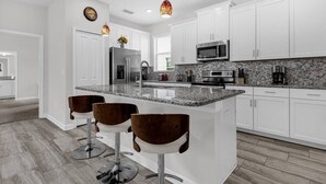 A modern kitchen with white cabinets, granite countertops, stainless steel appliances, and bar stools. - Last Minute Disney Getaway! Private Pool & Themed Bedrooms. Book Now! #166559 (Orlando)
