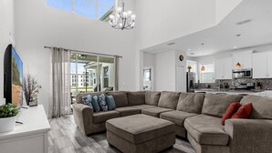 A spacious living room with a sectional sofa, a flat-screen TV, and a large window offering a view of the outside. - Last Minute Disney Getaway! Private Pool & Themed Bedrooms. Book Now! #166559 (Orlando)