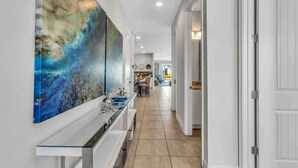 Un couloir qui donne sur un espace cuisine moderne, une table à manger et un grand tableau abstrait accroché au mur.