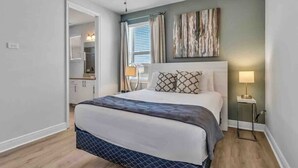 Une chambre à coucher avec un lit, un ventilateur de plafond, une table de chevet, une lampe et un tableau au mur.