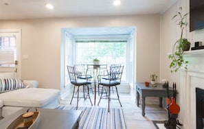 A modern living room with a sofa, a dining table with chairs, a fireplace, and a view through a window. - Parkside Retreat (Louisville)