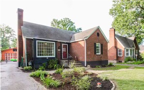 A two-story brick house with a front porch, a garage, and a well-maintained garden. - Parkside Retreat (Louisville)