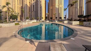 Una piscina con bordo piastrellato, circondata da un viale in pietra, con alti edifici residenziali sullo sfondo.