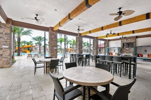 Ein Außenbereich mit einer Terrasse, runden Tischen und Stühlen, einem Pool mit Rutschen und einer Bar mit Sitzgelegenheiten.