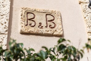 Uma placa de pedra com 'B&B' gravado, fixada numa parede com textura.