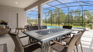Eine überdachte Terrasse im Freien mit Pool, Korbmöbeln und Blick auf Bäume.