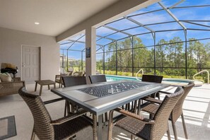 Eine überdachte Terrasse im Freien mit Pool, Korbmöbeln und Blick auf Bäume.