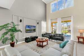A spacious living room with a large window, a flat-screen TV, a coffee table, and a potted plant. - Last Minute Disney Getaway! Private Pool & Themed Bedrooms. Book Now! #166721 (Orlando)