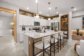 A modern kitchen with white cabinetry, stainless steel appliances, and a central island with bar stools. - Last Minute Disney Getaway! Private Pool & Themed Bedrooms. Book Now! #167327 (Orlando)