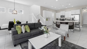 Una sala de estar moderna con un sofá gris, una mesa de centro blanca y un comedor con una cocina al fondo.