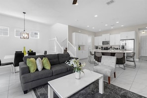 Ein modernes Wohnzimmer mit grauem Sofa, einem weißen Couchtisch und einem Essbereich mit Küche im Hintergrund.