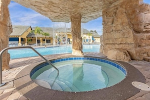 Ein Whirlpool mit Schwimmbad im Hintergrund, umgeben von Steinsäulen.