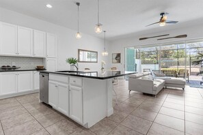 A spacious kitchen with white cabinetry, a large island, pendant lighting, and a view to an outdoor patio area. - Last Minute Disney Getaway! Private Pool & Themed Bedrooms. Book Now! #166597 (Orlando)