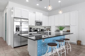 A modern kitchen with white cabinetry, stainless steel appliances, a black countertop, and a blue patterned backsplash. - Last Minute Disney Getaway! Private Pool & Themed Bedrooms. Book Now! #166597 (Orlando)