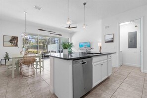 A modern kitchen with a central island, a dining area with wicker chairs, and a ceiling fan. - Last Minute Disney Getaway! Private Pool & Themed Bedrooms. Book Now! #166597 (Orlando)
