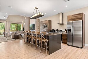 A modern kitchen with a stainless steel refrigerator, wooden cabinets, and a bar area with stools. - Last Minute Disney Getaway! Private Hot Tub & Modern Townhouse. Book Now! #166731 (Orlando)