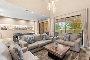A modern living room with a pool table, two sofas, a coffee table, and large windows with curtains. - Last Minute Disney Getaway! Private Hot Tub & Modern Townhouse. Book Now! #166731 (Orlando)