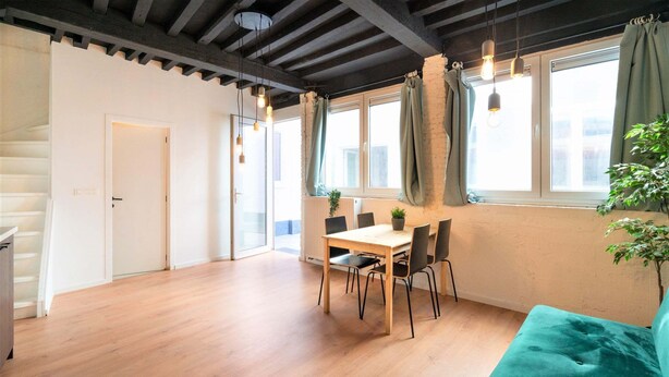 A spacious room with a wooden floor, a dining table with chairs, a teal sofa, and large windows with curtains. - Saint Pauls Deluxe Apartment (Antwerp)
