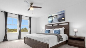 Un dormitorio con una cama grande, un ventilador de techo, una mesita de noche, un cuadro y una ventana con cortinas.