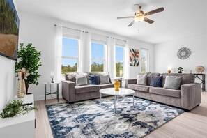 A modern living room with two grey sofas, a round coffee table, a ceiling fan, and large windows. - Last Minute Disney Getaway! Modern Spacious Townhouse. Book Now! #167211 (Orlando)