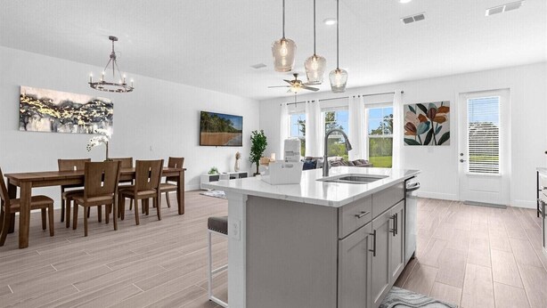 Una cocina moderna con una isla central, iluminación colgante y un comedor con sillas de madera.