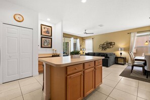 A modern kitchen with a central island, a dining area with a table and chairs, a sofa, and a ceiling fan. - Last Minute Disney Getaway! Private Pool & Comfortable Bedrooms. Book Now! #167221 (Orlando)