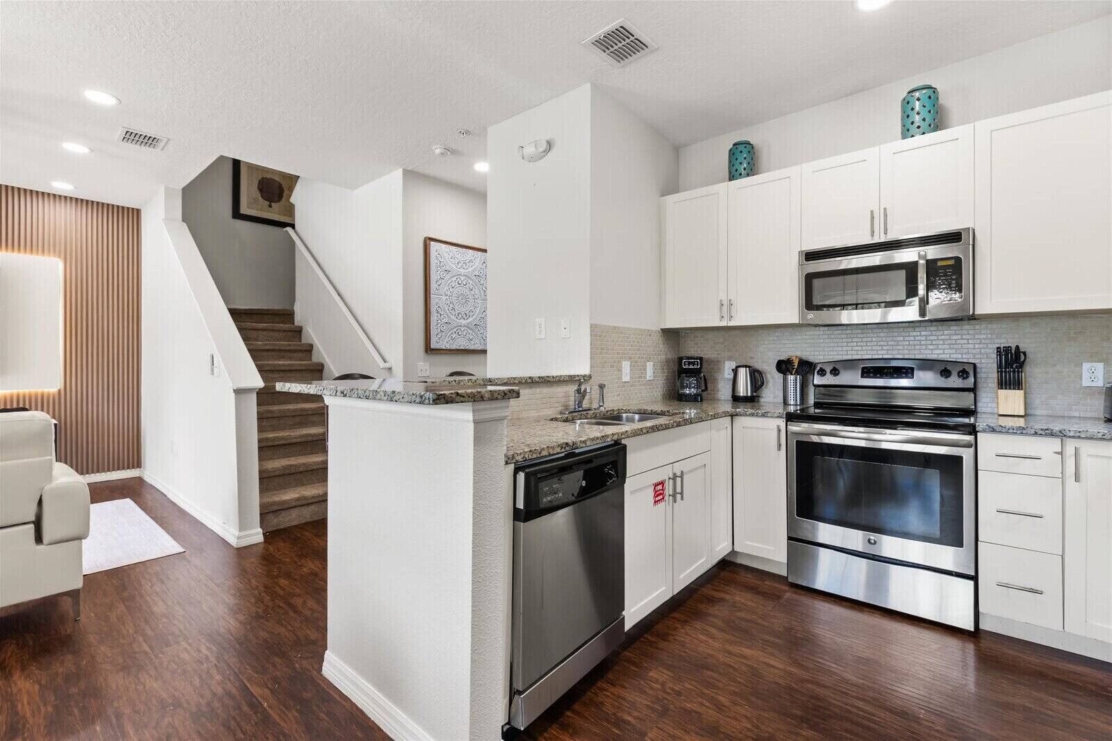 A modern kitchen with white cabinets, stainless steel appliances, a granite countertop, and a wooden staircase.