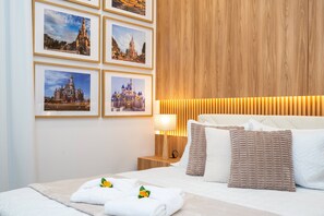 Ein Hotelzimmer mit einem Bett, Kissen, einem Nachttisch, einer Lampe und gerahmten Bildern an der Wand.