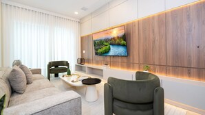 Una sala de estar moderna con un televisor de pantalla plana grande montado en una pared de madera, un sofá gris, un sillón verde y una pequeña mesa de centro.