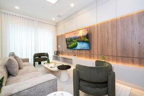 Ein modernes Wohnzimmer mit einem großen Flachbildfernseher an einer Holzwand, einem grauen Sofa, einem grünen Sessel und einem kleinen Couchtisch.