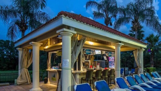 Un espacio de estar al aire libre cubierto con sillones reclinables, un bar y palmeras al fondo.