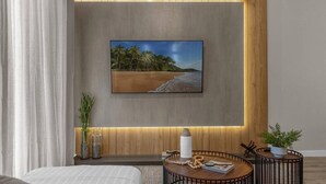 Ein modernes Hotelzimmer mit einem großen Fernseher, der an einer Wand aus Holzpaneelen befestigt ist, einem Nachttisch mit Lampe und einem kleinen runden Tisch mit Pflanze.