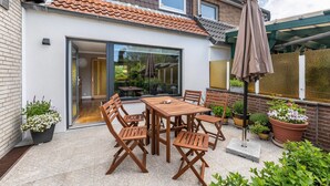 Une terrasse avec une table et des chaises en bois, des plantes en pot et un parasol.