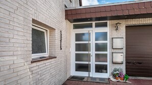 Un bâtiment en briques blanches avec une grande porte vitrée, une fenêtre et une porte de garage marron.