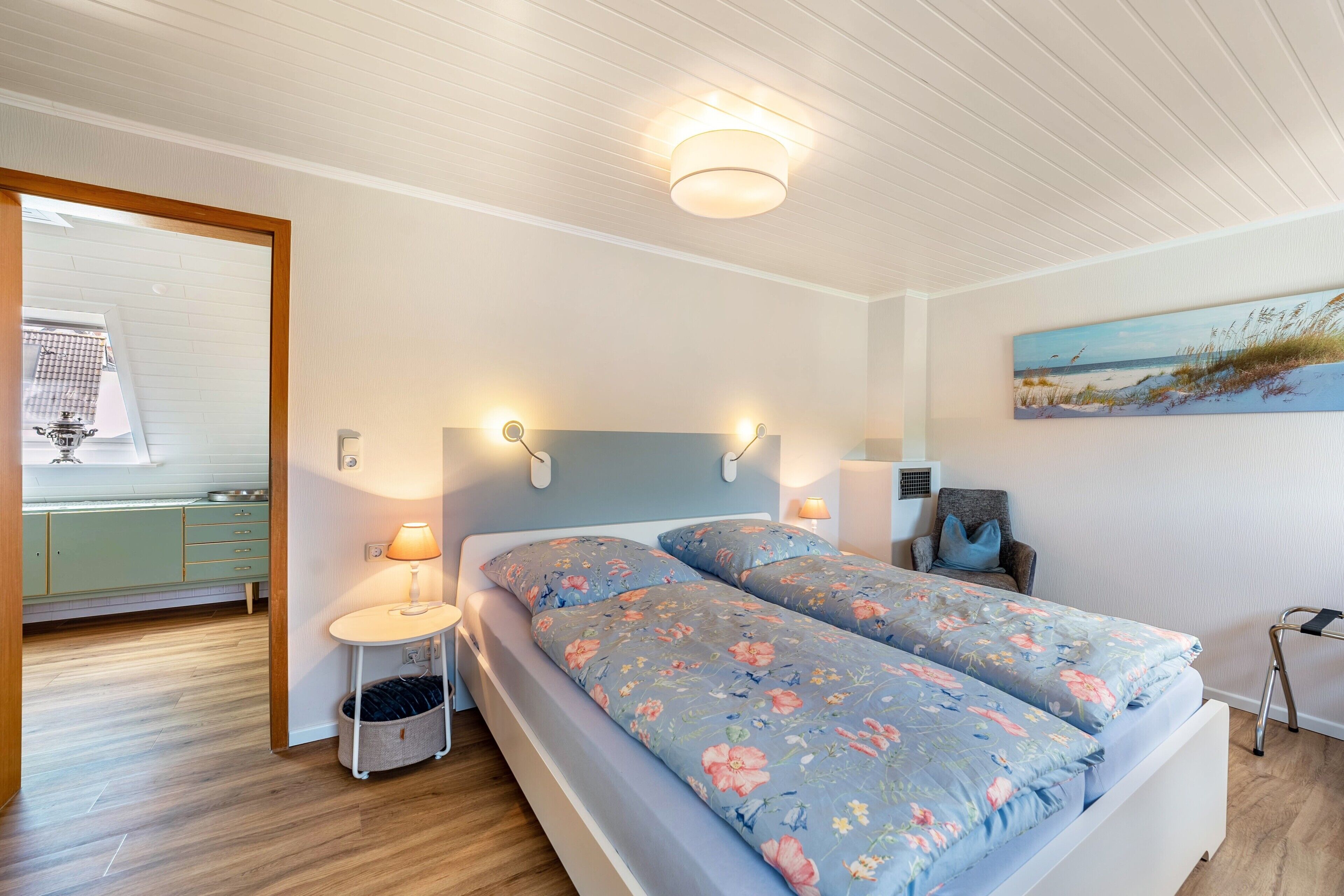 Ein Schlafzimmer mit einem Bett, Nachttischlampen, einem Sessel und einem Gemälde an der Wand.