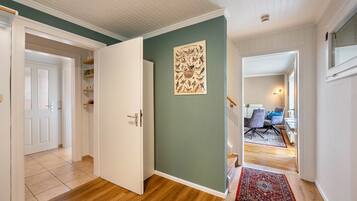 Un pasillo con suelo de madera, pared verde y una puerta que da a una habitación con una silla y una mesa.