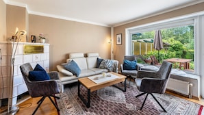 Un salon comprenant un canapé, deux fauteuils, une table basse et donnant sur un jardin grâce à une grande fenêtre.