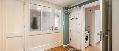 A hallway with a washing machine, a door with frosted glass panels, and a rug on the floor.