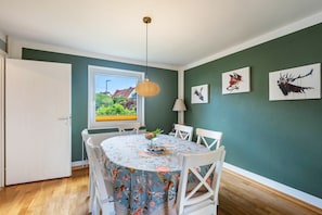 Een eethoek met een tafel gedekt voor vier personen, een raam met uitzicht op groen en twee dierenportretten aan de muur.
