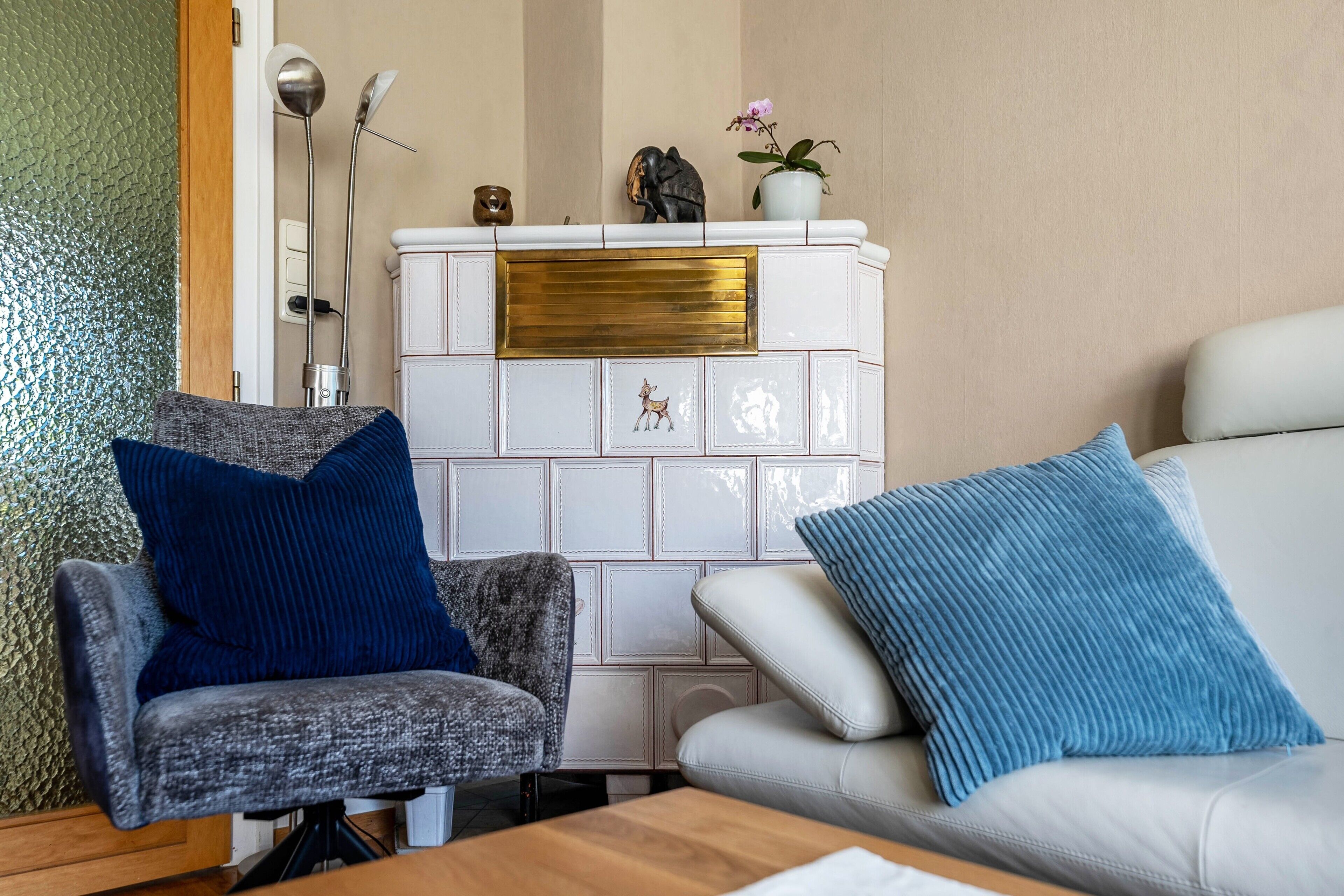 A living room with a white fireplace, a grey armchair, a white sofa, and a blue cushion.