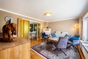Een woonkamer met een bank, stoelen, een houten salontafel, een vloerkleed, een klok en een beeldhouwwerk.