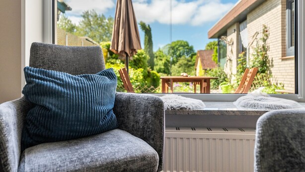 Une pièce avec vue sur un jardin, un coin fenêtre agrémenté d’un coussin et une chaise avec un coussin.