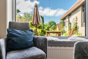 Een kamer met uitzicht op een tuin, een raamzit met kussen, en een fauteuil met kussen.