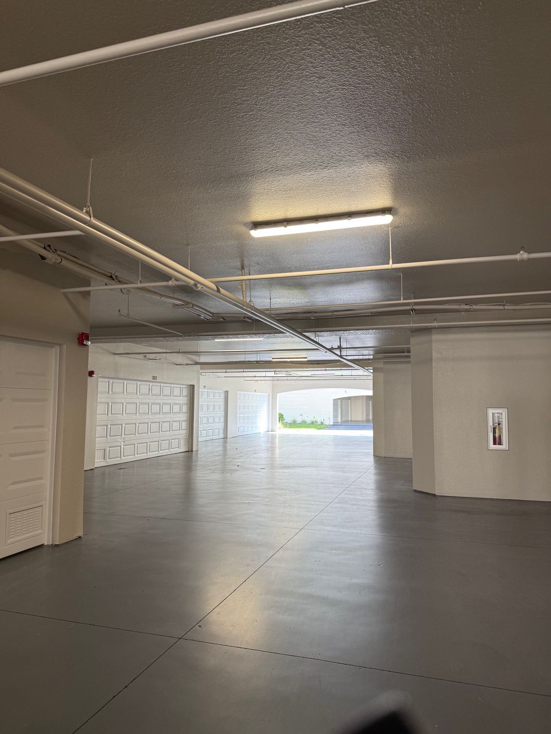 A spacious indoor parking area with multiple garage doors, overhead lighting, and visible ceiling pipes.