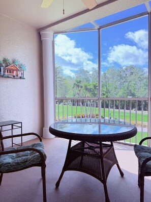 Ein Balkon mit einem Glastisch und zwei Korbstühlen, mit Blick auf eine grüne Landschaft.